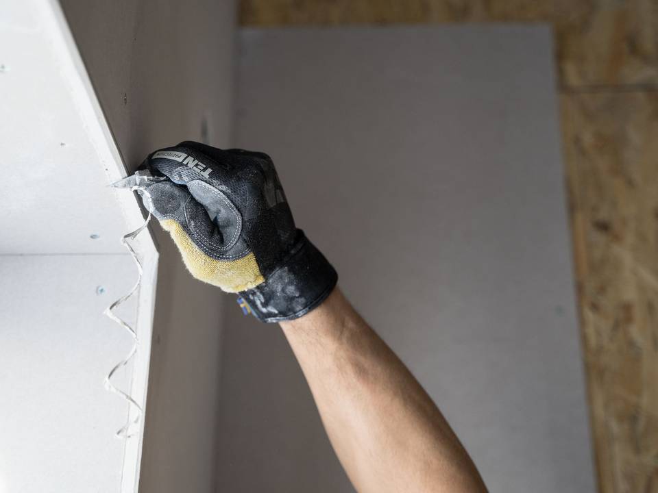 Mão de luva passando massa na junta de uma parede de drywall